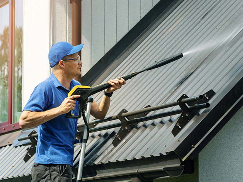 man on ladder pressure washing roof de forest wi